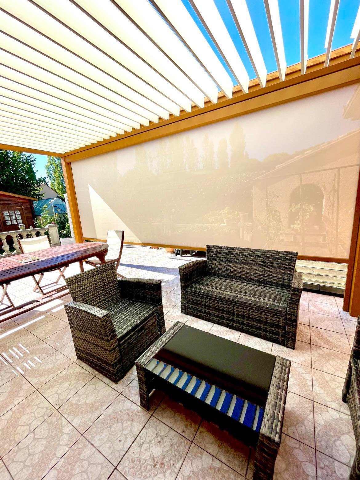 Terrasse moderne avec pergola bioclimatique, store enrouleur, salon de jardin et table à manger en bois.