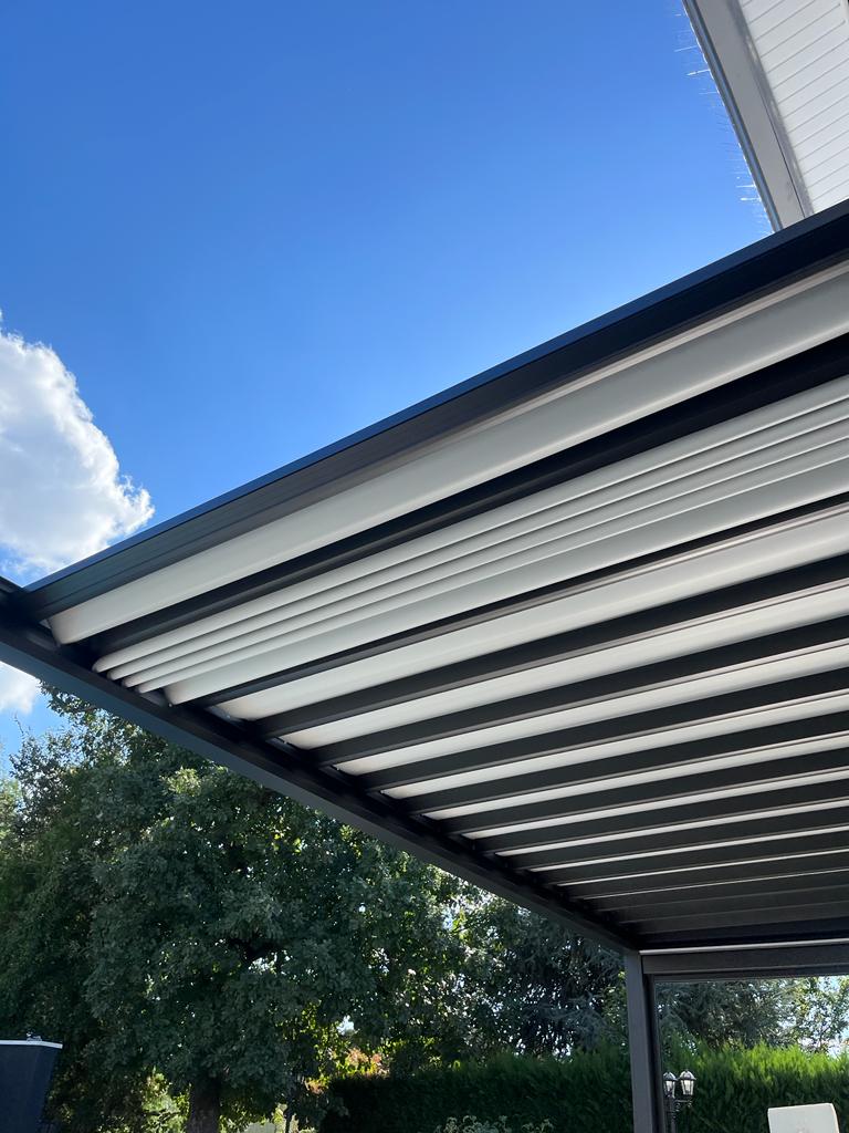 Pergola bioclimatique noire moderne avec lames orientables blanches et noires sous un ciel bleu nuageux.