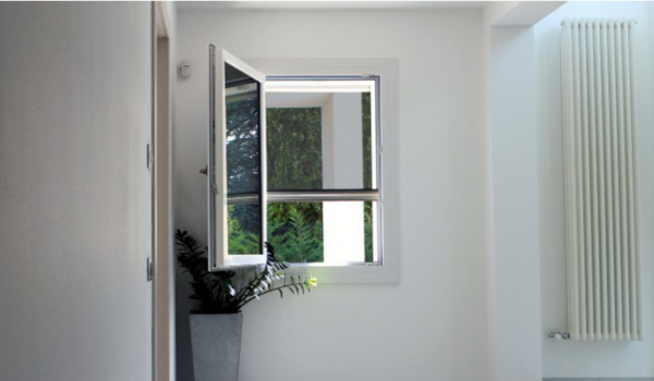 Intérieur blanc lumineux avec fenêtre ouverte vue sur arbres verts, une plante en pot et un grand radiateur blanc.