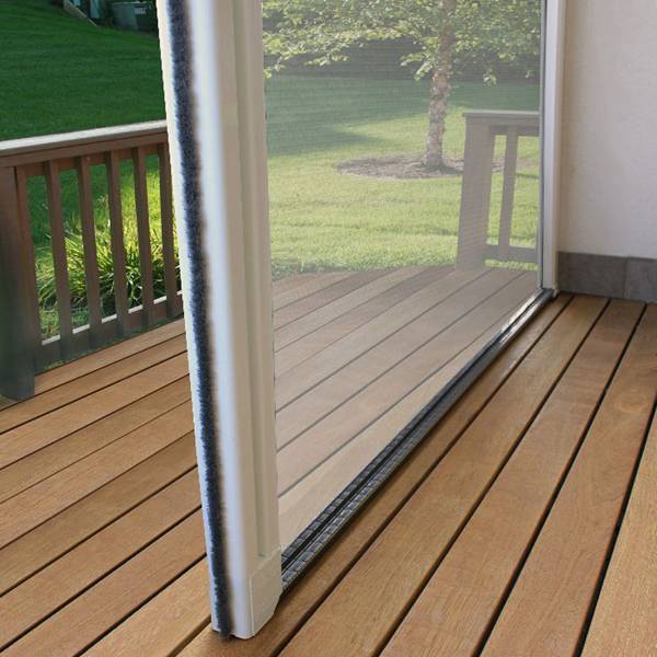 Porte moustiquaire rétractable blanche sur terrasse en bois, vue sur jardin. Détail du rail bas et du joint brosse.