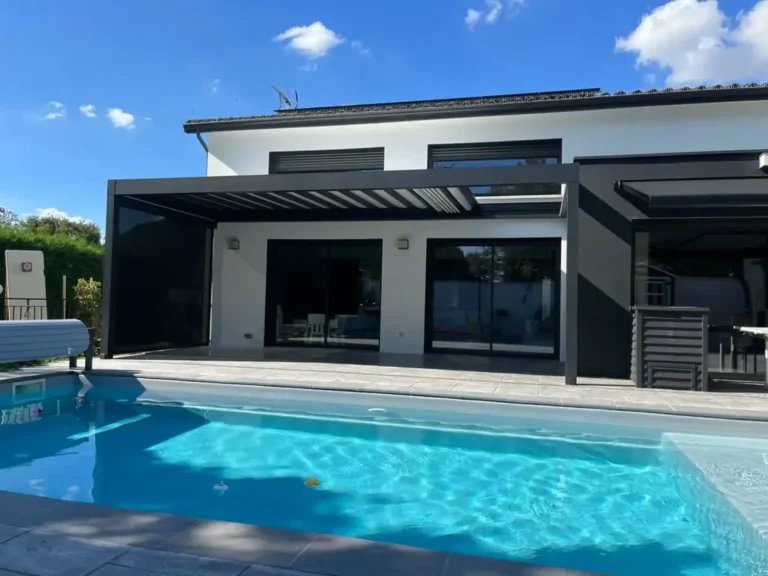 Maison contemporaine blanche avec pergola bioclimatique noire, piscine bleue et grande terrasse. Journée ensoleillée.