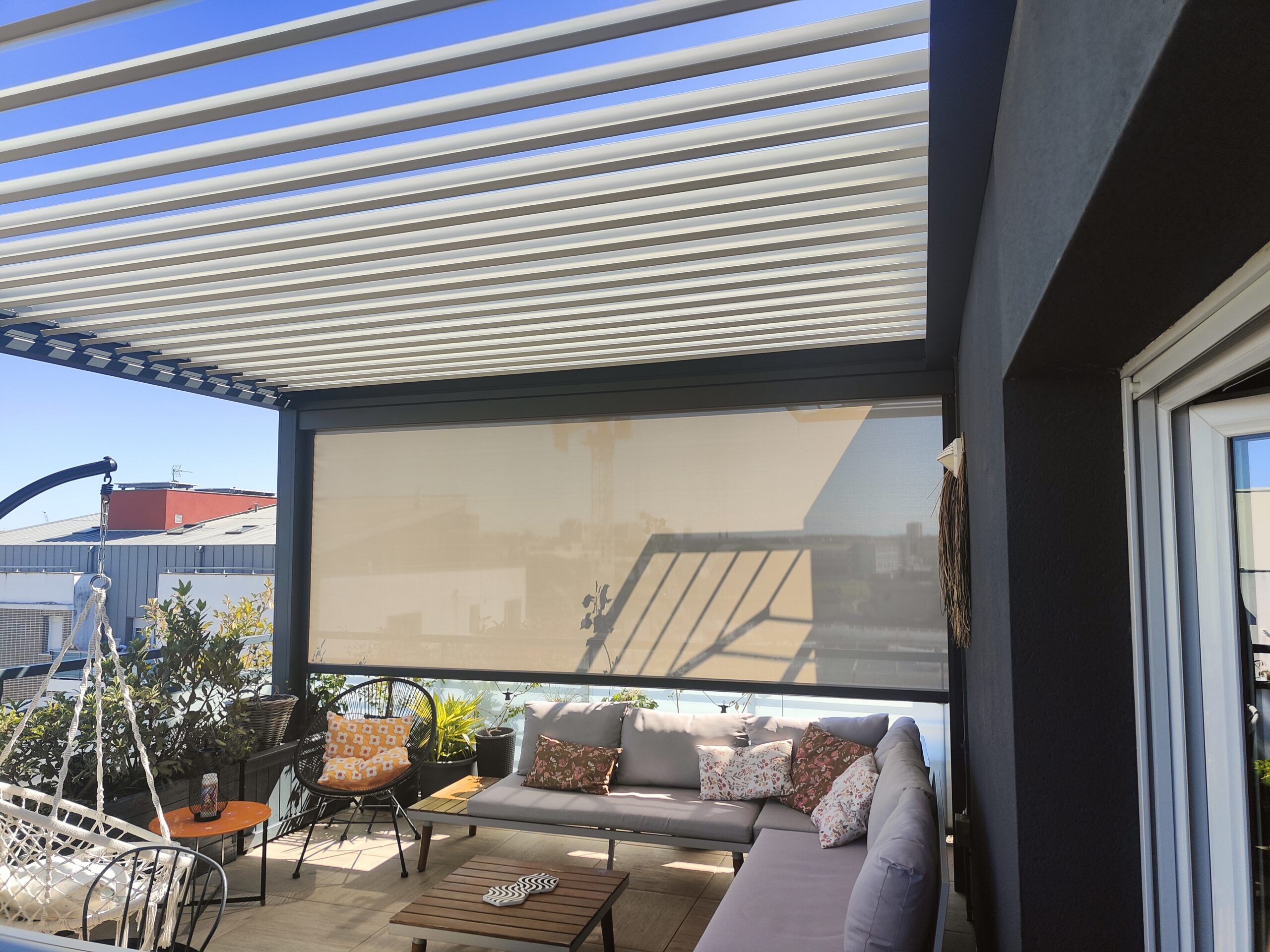 Terrasse avec pergola bioclimatique à lames, store rétractable et salon de jardin confortable avec coussins et plantes.