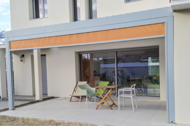 Pergola moderne grise avec bande orange sur terrasse carrelée, meublée pour profiter de l'extérieur d'une maison.