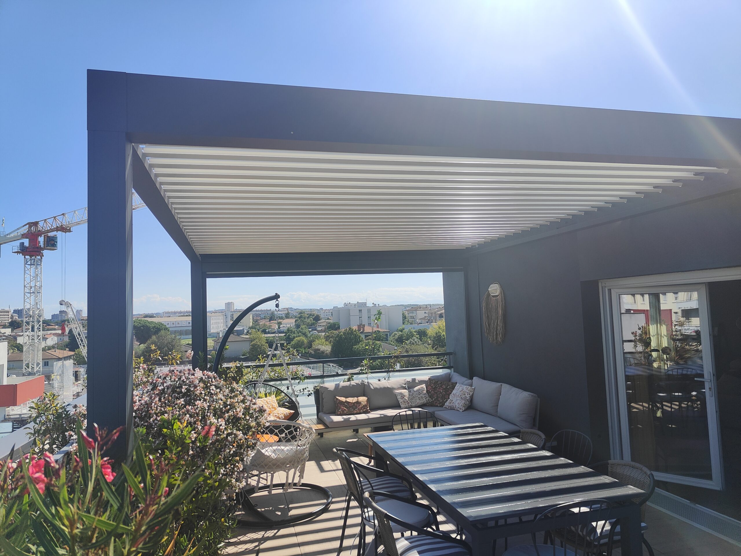 Terrasse sur le toit ensoleillée avec pergola moderne, salon de jardin, table à manger et vue imprenable sur la ville.