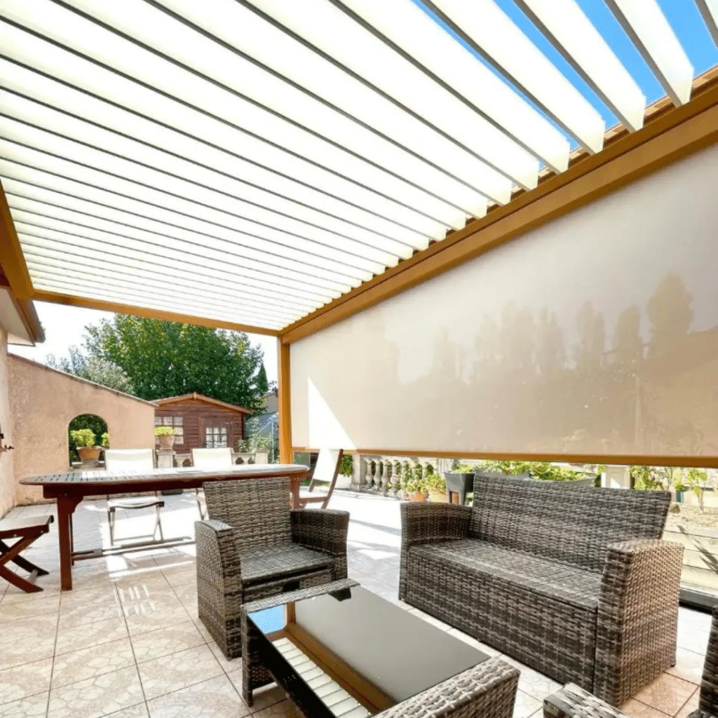 Pergola bioclimatique en bois sur terrasse carrelée, lames blanches orientables, store latéral beige, mobilier de jardin.