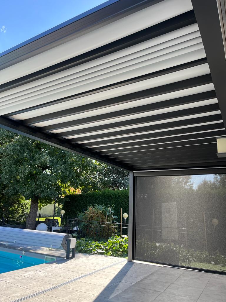 Pergola bioclimatique noire sur terrasse moderne près d'une piscine avec lames orientables et store latéral.