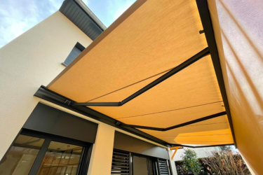 Store banne beige rétractable déployé sur une terrasse de maison, offrant une protection solaire efficace. Bras articulés.