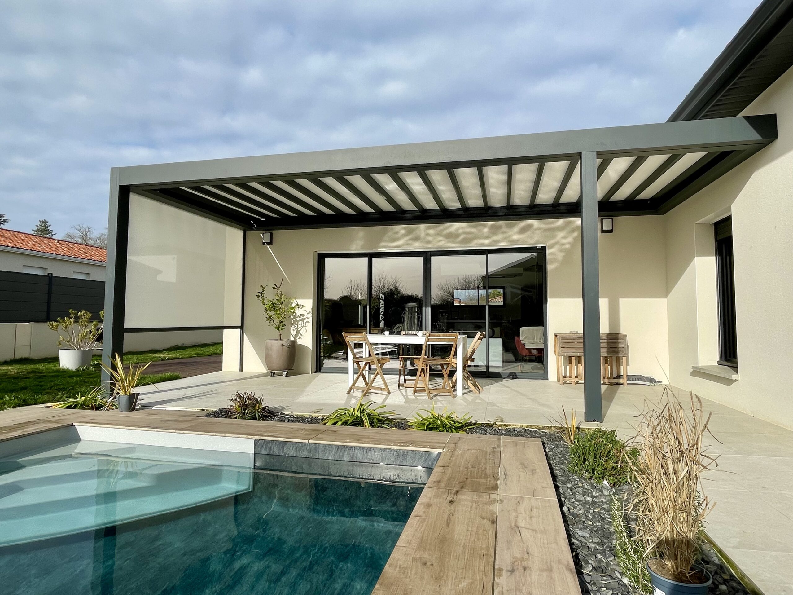 Terrasse moderne avec pergola bioclimatique grise, salon de jardin blanc et piscine intégrée.
