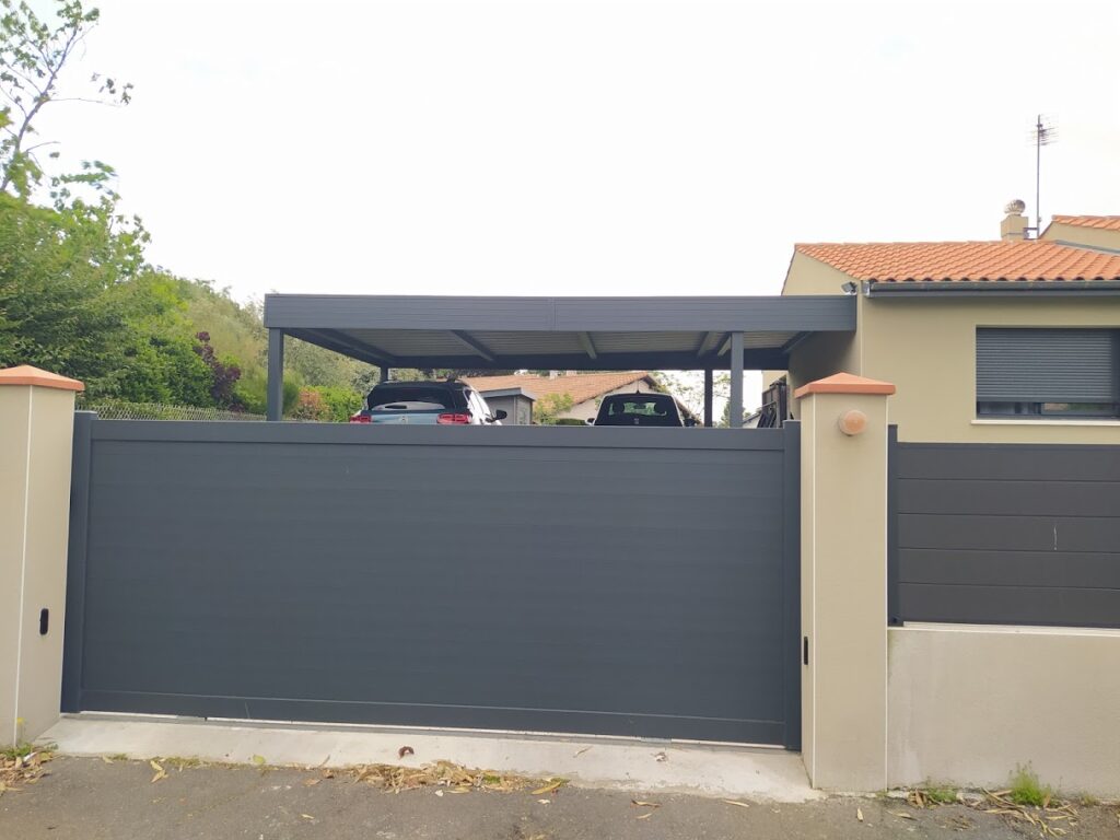 Entrée de maison moderne avec grand portail coulissant gris, carport et deux voitures.