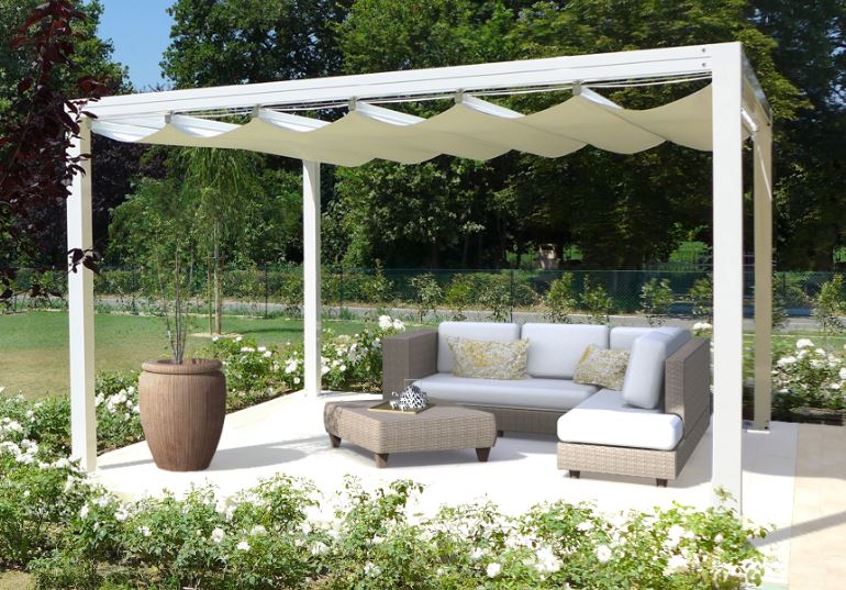Pergola blanche avec toile rétractable au-dessus d'un salon de jardin en rotin sur une terrasse entourée de roses blanches.