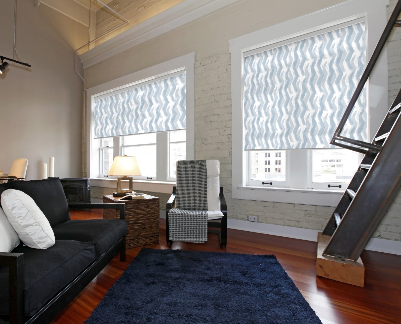 Salon moderne avec canapé noir, tapis bleu foncé, fauteuil blanc, mur en briques peintes et stores roulants bleus ondulés sur les fenêtres.