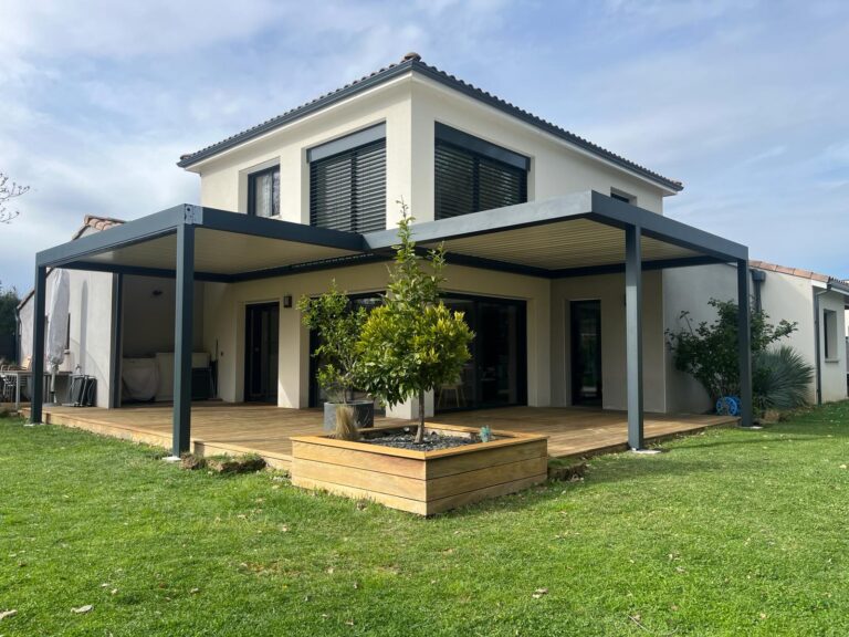 Grande maison moderne avec terrasse en bois et deux pergolas bioclimatiques gris foncé. Un jardin verdoyant entoure l'aménagement extérieur.
