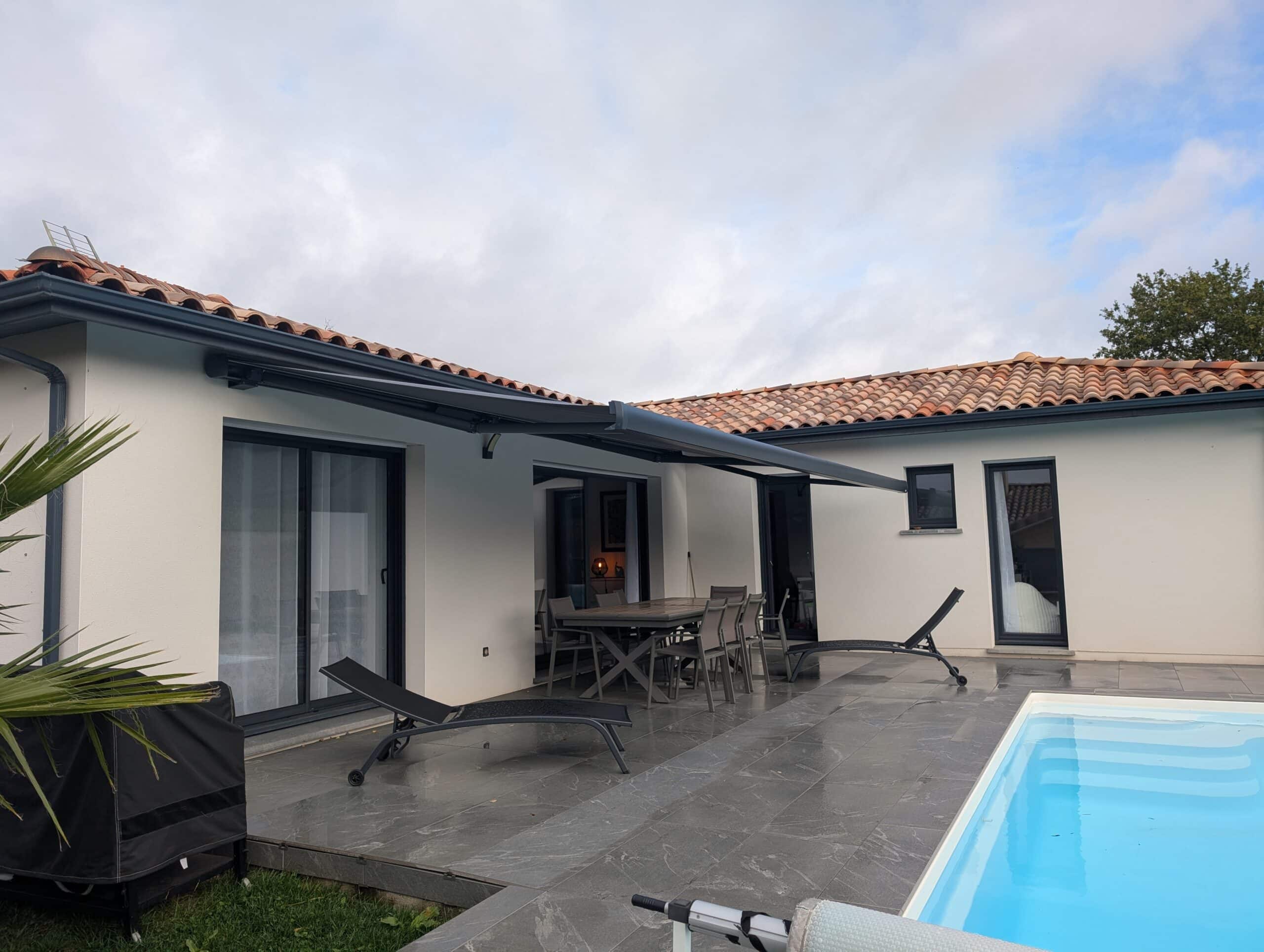 Terrasse moderne avec store banne déployé, mobilier d'extérieur, et piscine sous un ciel nuageux.