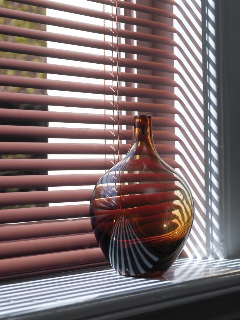 Des stores vénitiens marron créent des ombres rayées et un jeu de lumière intense.