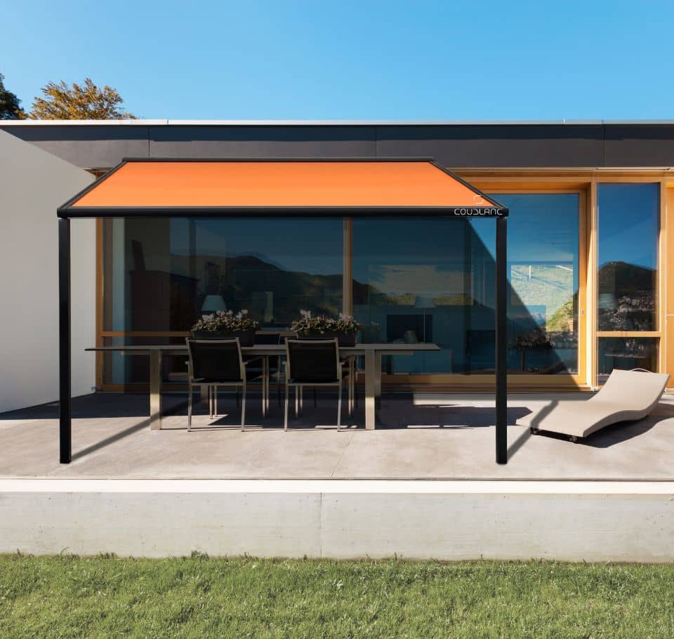 Pergola COUSLANC noire et store terrasse orange moderne protégeant un coin repas extérieur. Architecture contemporaine et pelouse verte.