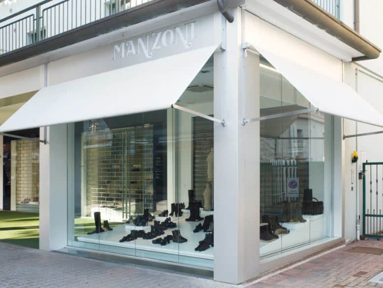 Vitrine de la boutique Manzoni avec auvents blancs et chaussures noires exposées de manière élégante.