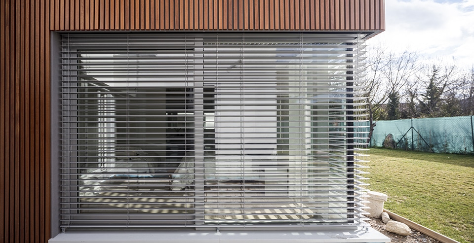 Brise-soleil orientable gris installé sur une façade en bois moderne avec vue sur un jardin.