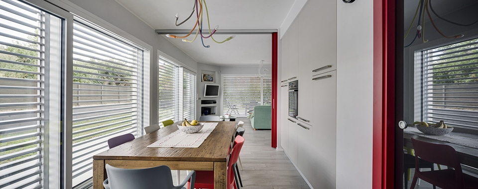 Salle à manger moderne avec table en bois, chaises colorées et grandes baies vitrées lumineuses.