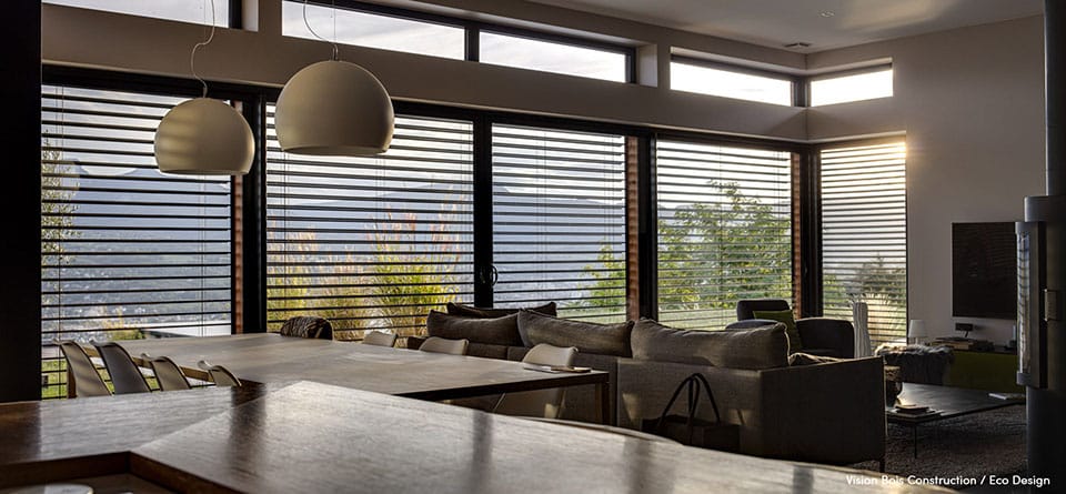 Intérieur moderne Vision Bois Construction avec grandes baies vitrées, stores à lamelles et vue sur les montagnes. Brise-soleil Lamisol