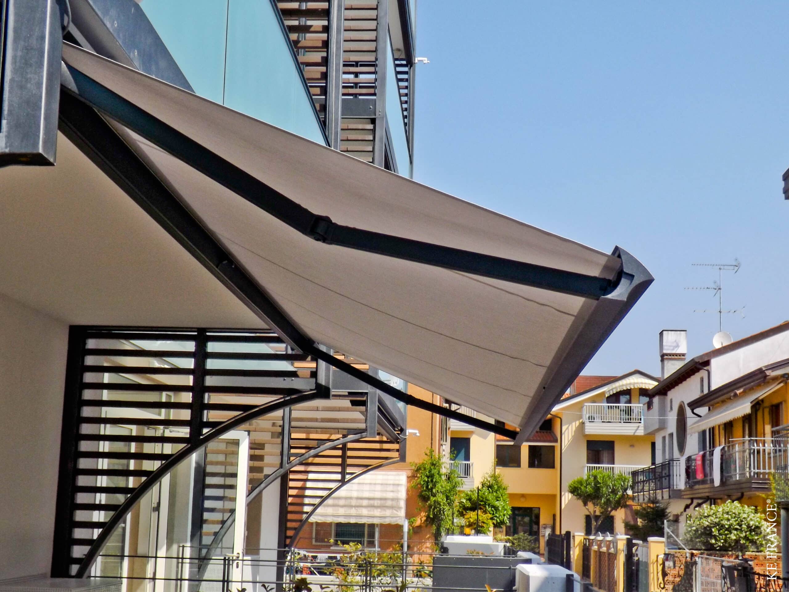Store banne gris à bras articulés KE France installé sur une terrasse moderne ensoleillée.