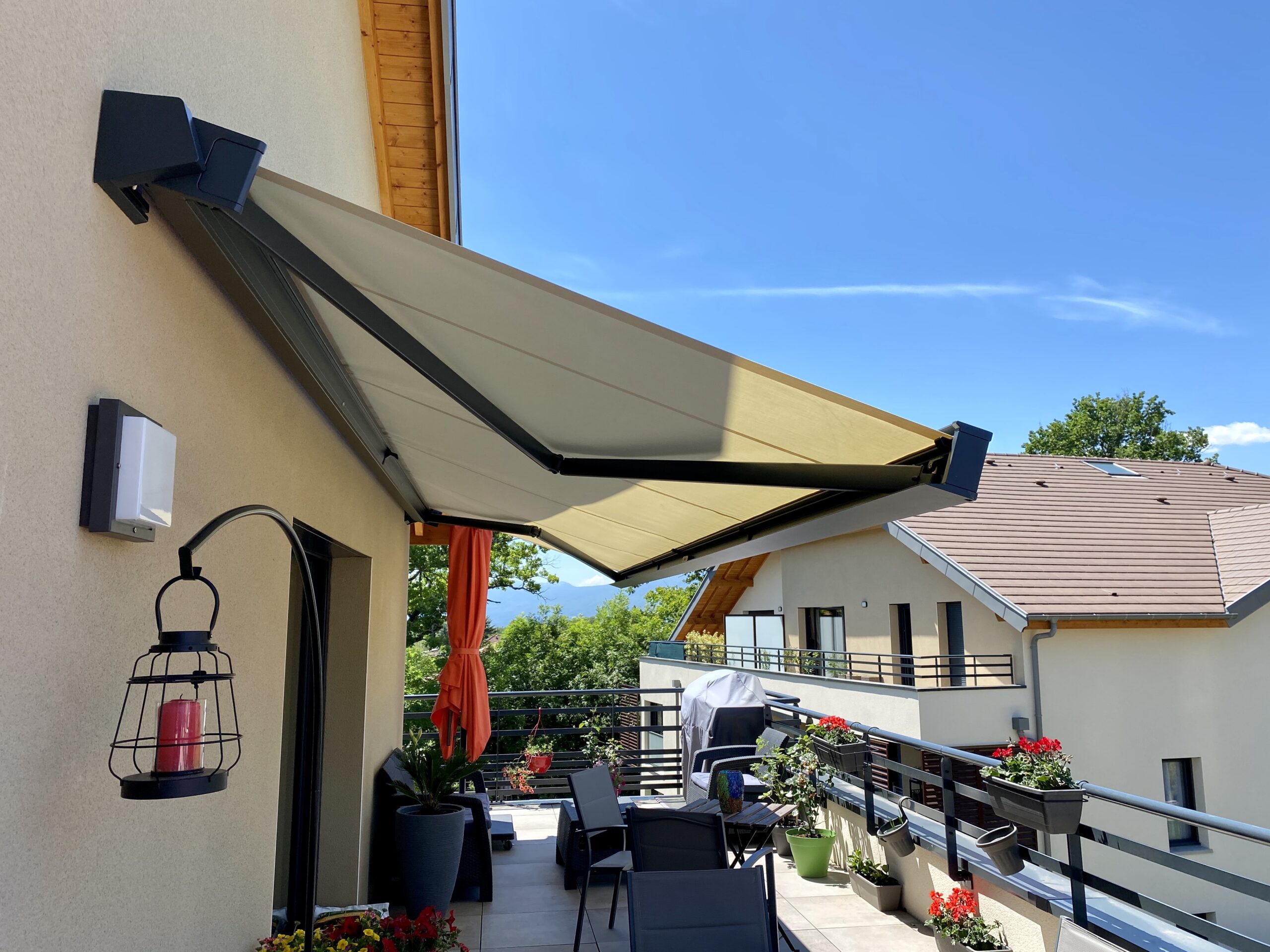 Store banne motorisé sur une terrasse moderne avec mobilier de jardin et fleurs sous un ciel bleu.