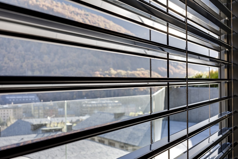 Brise-soleil Lamisol extérieurs en métal noir offrant une vue floue sur une ville et des montagnes en automne.