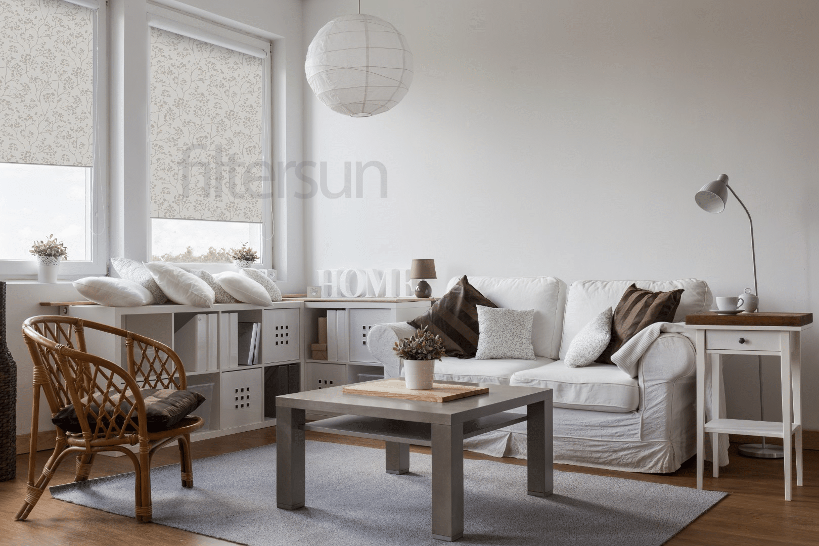 Salon lumineux avec canapé blanc, stores enrouleurs motifs fleurs Filtersun, déco Home, table basse grise et fauteuil rotin.